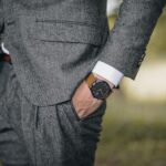 Close-up of a man in a tailored suit wearing an elegant wristwatch outdoors, exuding fashion and sophistication.
